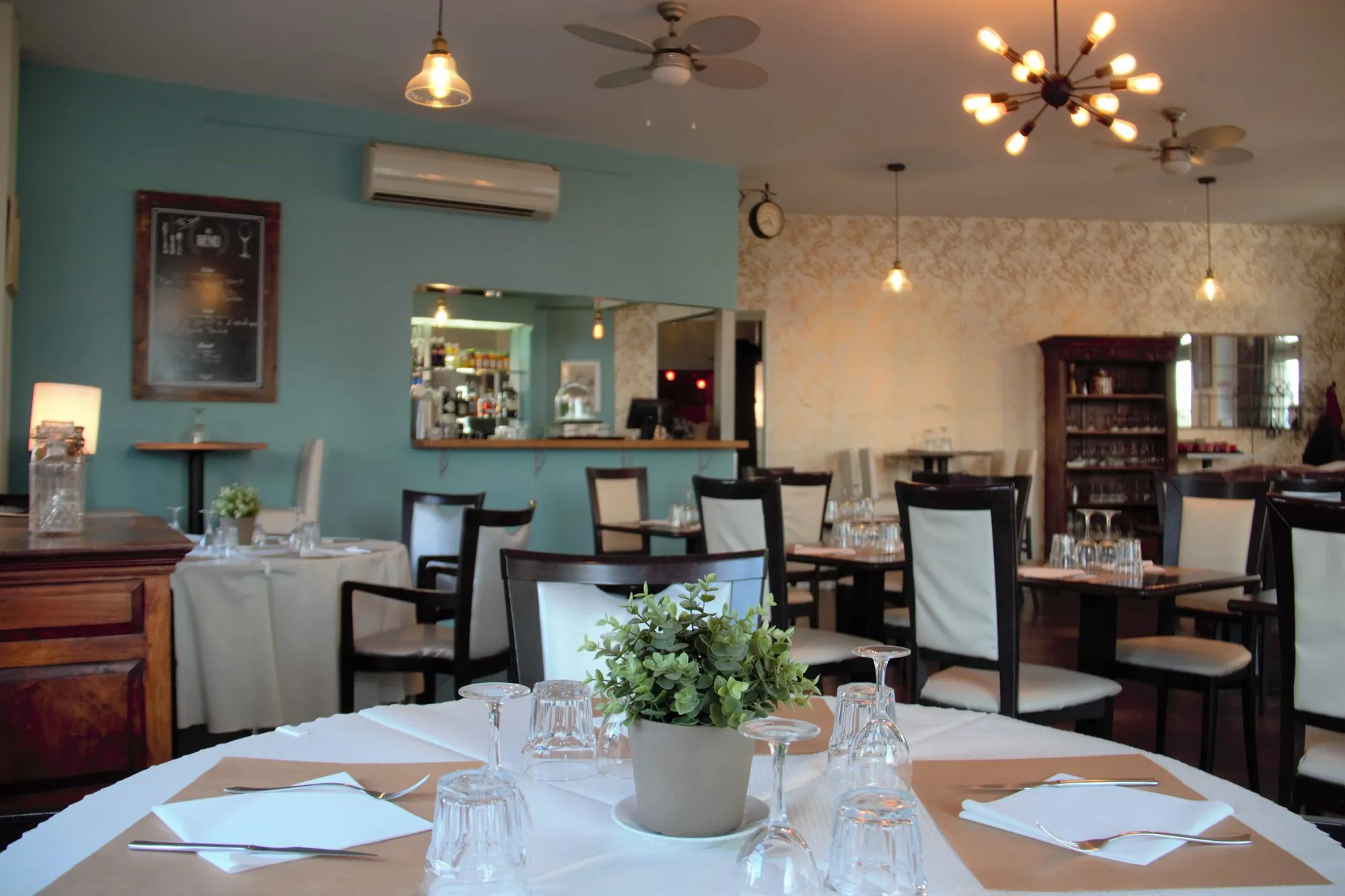 La salle lumineuse du bistrot, murs vert-de-gris et tables dressées